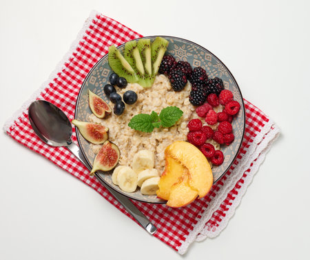 boiled oatmeal with fruit in a round plate on a white table, healthy breakfast. View from aboveの写真素材