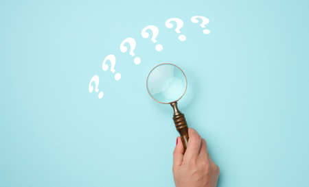 female hand holds a plastic magnifying glass and question marks on a blue background. The concept of finding an answer to questions, truth and uncertainty.の写真素材