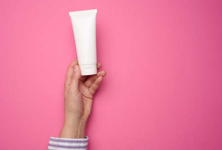 female hand holding white plastic tube. Packaging for cream, gel, serum, advertising and product promotionの写真素材