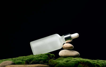 white glass bottle with pipette stands on green moss, black background. Cosmetics SPA branding. Packaging for gel, serum, advertising and product promotion, mock upの写真素材
