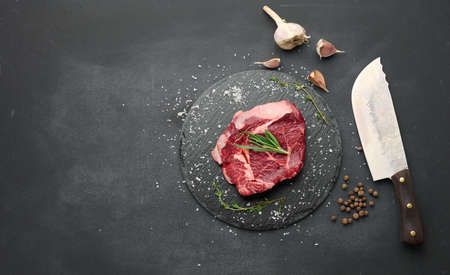 raw piece of beef ribeye with rosemary, thyme on a black table, top viewの写真素材