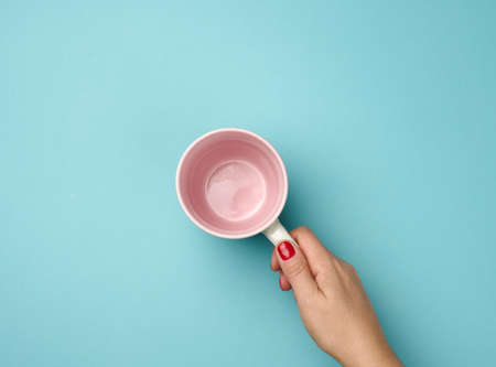 female hand holds a gray empty ceramic mug on a blue background, break time and drink coffee, top viewの写真素材