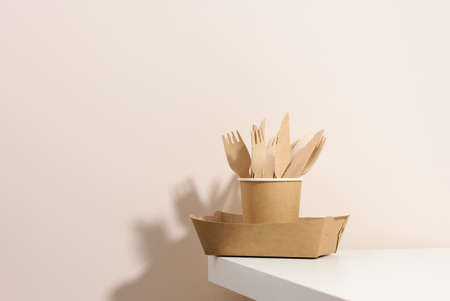 paper cardboard brown plates and cups, wooden forks and knives on a white table, beige background. Eco-friendly tableware, zero wasteの写真素材