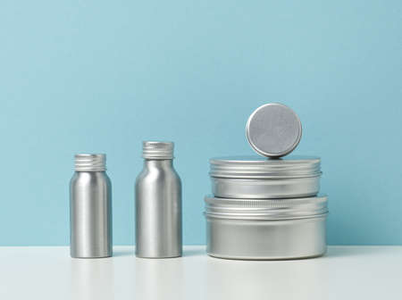 empty silver metal bottle for cosmetics on white table, blue background. Packaging for cream, gel,...