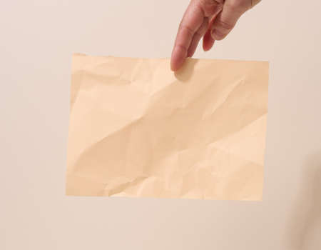 female hand holds a crumpled sheet of paper on a beige background. Place for inscriptions and announcementsの写真素材