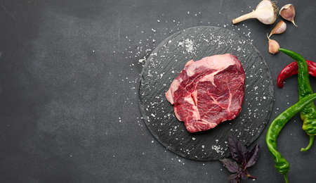 raw piece of beef ribeye with rosemary, thyme on a black table, top view, copy spaceの写真素材