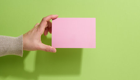 Female hand holding empty pink paper on a green background. Copy paste image or text, close upの写真素材