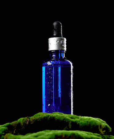 blue glass bottle with pipette stands on green moss, black background. Cosmetics SPA branding mockupの写真素材