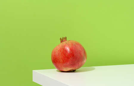 whole ripe red pomegranate on white table, green backgroundの写真素材