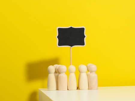 group of wooden figurines and a blank signpost on a yellow background. The concept of gathering people to express their will, demonstration, rally and strikeの写真素材