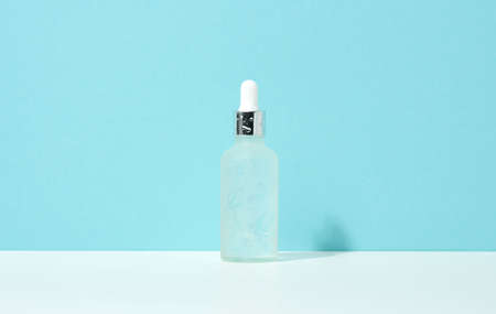 white glass bottle with pipette stands on a blue background. Cosmetics SPA branding. Packaging for...