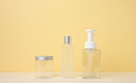 cream tubes, cosmetic dispenser, empty plastic jar, transparent dispenser on a light yellow background. Branding of cosmetic products, mock upの写真素材
