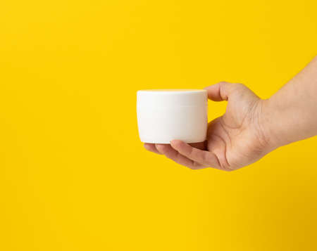 female hand holds empty white jar for cosmetics. Packaging for cream, gel, serum, advertising and product promotion, mock upの写真素材