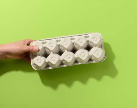 hand hold paper rectangular tray for chicken eggs on a green background, close up