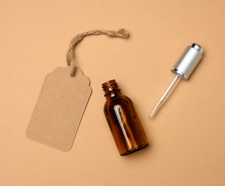 paper tag and glass cosmetic brown bottle with a pipette on a beige background. Cosmetics SPA branding mockup, top viewの写真素材