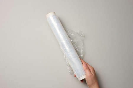 two female hands hold a roll of transparent cling film for packaging products, gray backgroundの写真素材