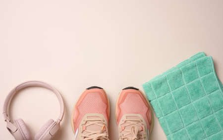 pair of pink textile sneakers, wireless headphones and a textile green towel on a beige background. Set for sports, runningの写真素材
