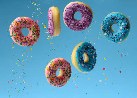 sweet multicolored donuts levitate on a blue background, sugar sprinkles are flying aroundの写真素材