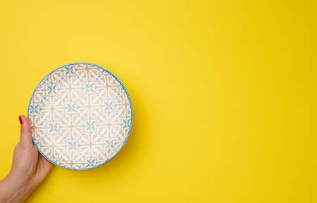 female hand holding an empty round plate on a yellow background, top viewの写真素材