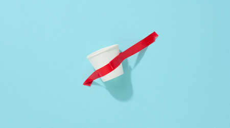 white cardboard cup glued with red sticky tape to the blue backgroundの写真素材