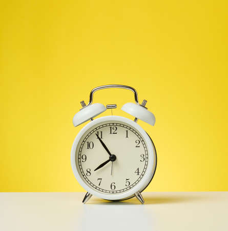 round white alarm clock, five minutes to eight in the morning. Yellow backgroundの写真素材