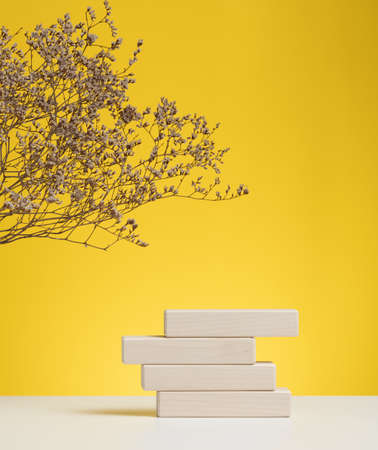 wooden podium to showcase cosmetics and other items, yellow background with dry wildflowers and...