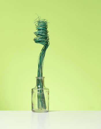glass transparent vase with green dried flowers on a white table, green background
