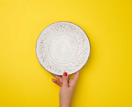 female hand holding white empty round plate on a yellow background, top viewの写真素材