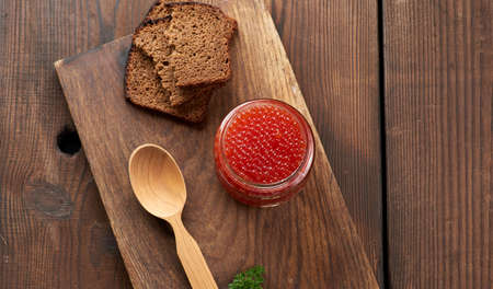 full glass jar with red caviar on a brown wooden table, top view