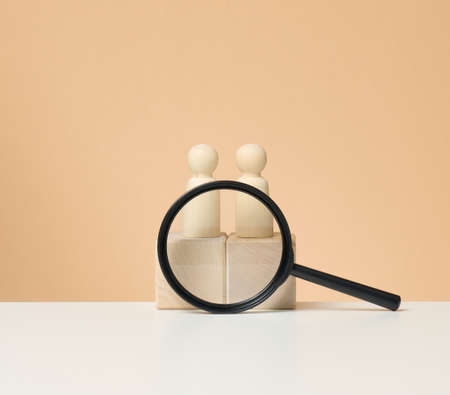 wooden figures of men stand on a beige background and a red plastic magnifying glass. Recruitment concept, search for talented and capable employees, career growthの写真素材