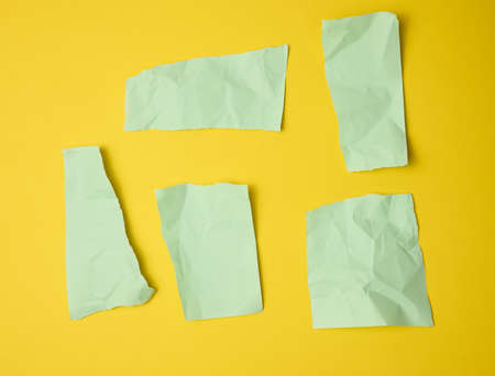 various torn green pieces of paper on yellow background, flat lay
