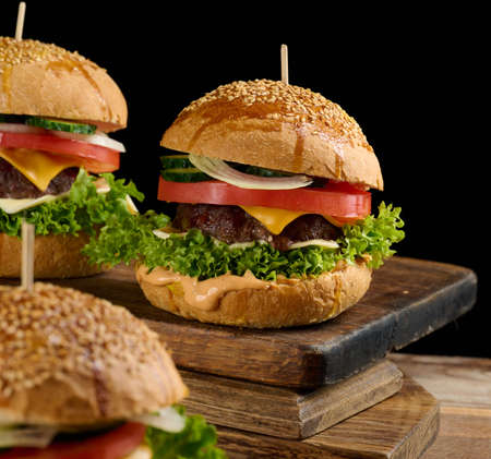 cheeseburger with grilled beef patty, cheddar cheese, tomato and lettuce on a wooden board, black background