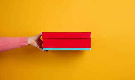 female hand holding a red cardboard box on a yellow background, deliveryの写真素材