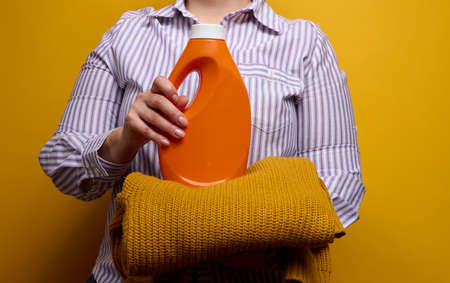 a woman in a white striped shirt holds an orange plastic bottle with liquid washing gel and a...