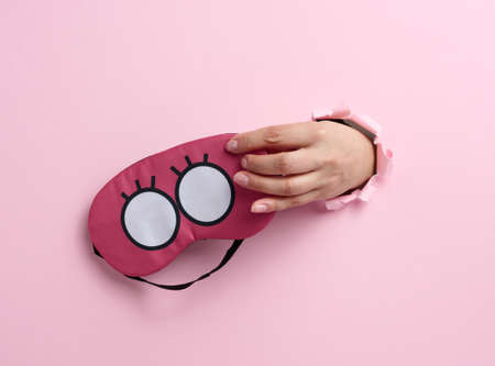 pink textile sleep mask in a female hand sticking out of a bull in a pink paper background, insomniaの写真素材