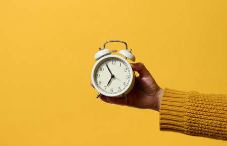 round alarm clock in a woman's hand, the time is five minutes to seven in the morning. Yellow backgroundの写真素材