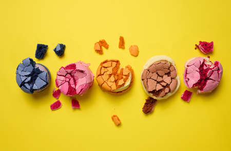 broken round macarons with crumbs on a yellow background, delicious dessert, top viewの写真素材