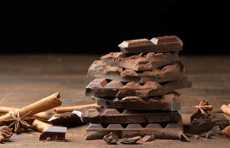 broken pieces of dark chocolate, cinnamon sticks and star anise on a brown wooden tableの写真素材
