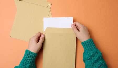 female hand holds paper envelopes on an orange background, top view. Correspondenceの写真素材