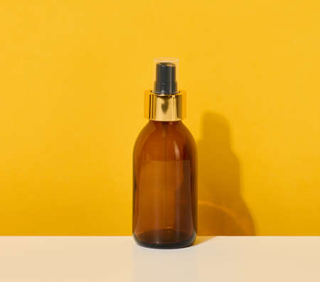 glass brown bottle with cosmetic spray on a yellow backgroundの写真素材