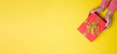 two female hands are holding red gift box on a yellow background, concept of congratulations on...