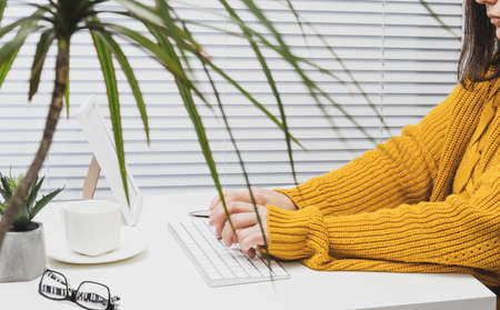 a woman in an orange sweater sits at a table and works at a computer. Remote work, freelance. Online...
