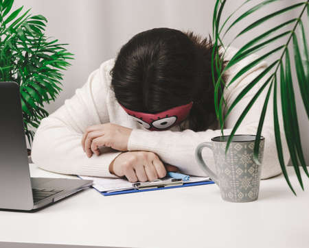 woman in a sweater sleeps at a work table, next to a laptop. Fatigue and overwork concept. Laziness