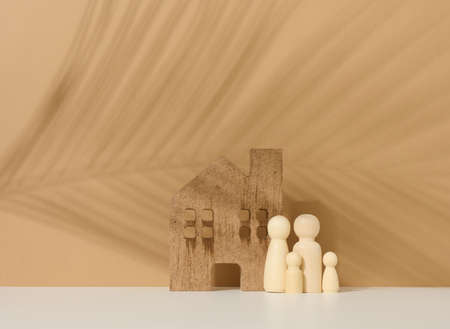 wooden family figurines, model house on a brown background. Real estate purchase, rental concept. Moving to new apartmentsの写真素材