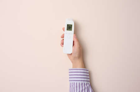 female hand holding a plastic non-contact thermometer on a beige backgroundの写真素材
