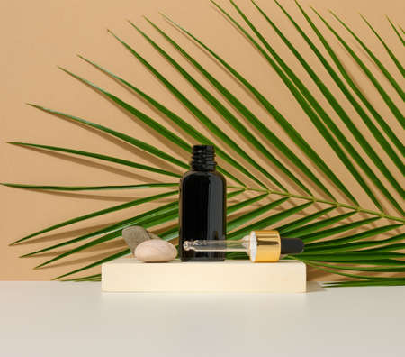 brown glass bottle with a pipette stands on a brown background. Container for cosmetics, serum and...