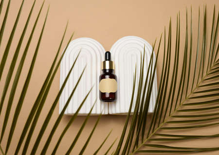glass brown bottle with pipette and paper blank label on light brown background, near palm leaf. Mockup skincare cosmetic productの写真素材