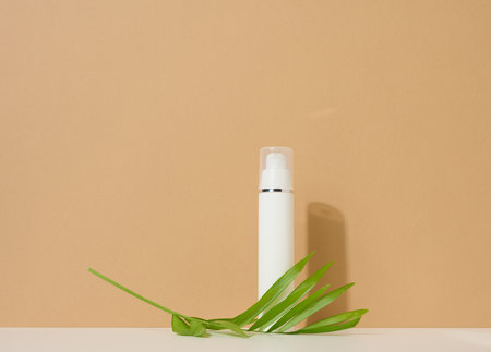 white plastic cosmetic bottle with dispenser and transparent cap on brown background. Packaging for cream, fluid and gelの写真素材