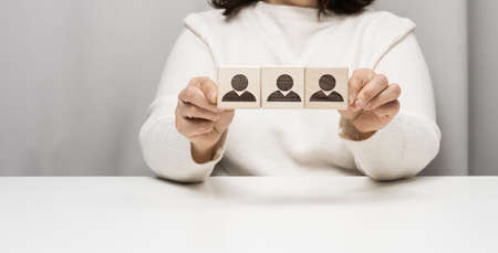woman sits at a table and holds wooden cubes. The concept of recruiting a team in business, finding talented employees. Leader in a group of peopleの写真素材