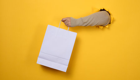 female hand holds a white paper disposable bag with handles for groceries and clothes. Recyclable packaging. Zero waste. Saleの写真素材